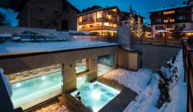 Luxurious mountain hotel in winter with outdoor heated pool, snow-covered surroundings, cozy chalet-style architecture, and festive lights in a picturesque alpine village.