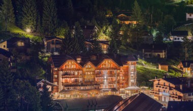 Charming illuminated alpine lodge at night in Alto.Ski resort, nestled in a pine forest with mountain views, showcasing luxury skiing accommodation and winter holiday comfort.